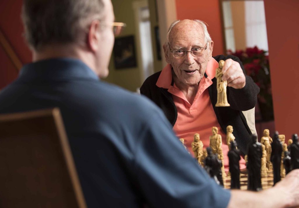 An elderly man wins at chess against his caregiver.